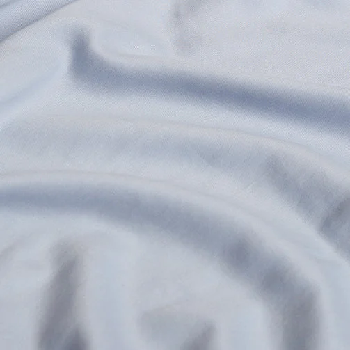 Close-up van een lichtblauw hoeslaken, zacht TENCEL materiaal. Het laken is gedrapeerd met subtiele plooien en een zachte textuur.