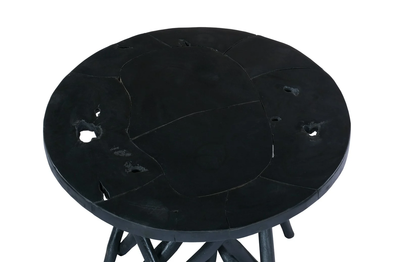 De Bijzettafel Zwart Teakhout is een ronde zwarte teakhout tafel met een gebarsten, oneffen oppervlak met verschillende gaten. Ondersteund door donkere poten heeft het een ruwe, organische uitstraling en een abstract ontwerp.