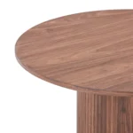 Een close-up van de Nora Bijzettafel - Ø60cm Walnoot benadrukt het ronde walnoten tafelblad met zichtbare houtnerf en een deel van het cilindrische onderstel.