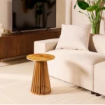 Een moderne woonkamer met een witte bank, de bijzettafel Phiel - Naturel Ø40cm, een grote tv op een houten console en een groene plant op de achtergrond. De inrichting is minimaal en gezellig.