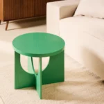 De bijzettafel Oscar - Groen Ø50cm, een klein rond groen tafeltje met modern design, staat op een lichtgekleurd vloerkleed naast een beige bank in de woonkamer.