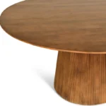 De Mokka Ronde Eettafel Lichtbruin - Ø150cm is een ronde houten tafel met een glad blad en een breed, cilindervormig, geribbeld onderstel, afgebeeld tegen een witte achtergrond.