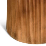Close-up van de onderkant van de Mokka Ronde Eettafel Lichtbruin (Ø150cm), met een cilindrische, verticaal geribbelde, warmbruine basis die een schaduw werpt op een wit oppervlak.