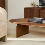 Een moderne woonkamer met een lichtbeige fauteuil, een Mangohout Design Salontafel 78 x 38 CM met gestapelde boeken en een houten mediaconsole op de achtergrond.