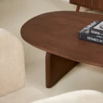 De Salontafel 78 x 38 CM Mangohout, met een industrieel ontwerp, staat in een moderne woonkamer, omringd door beige gestoffeerde stoelen op een lichte vloer, met daarbovenop een boek.