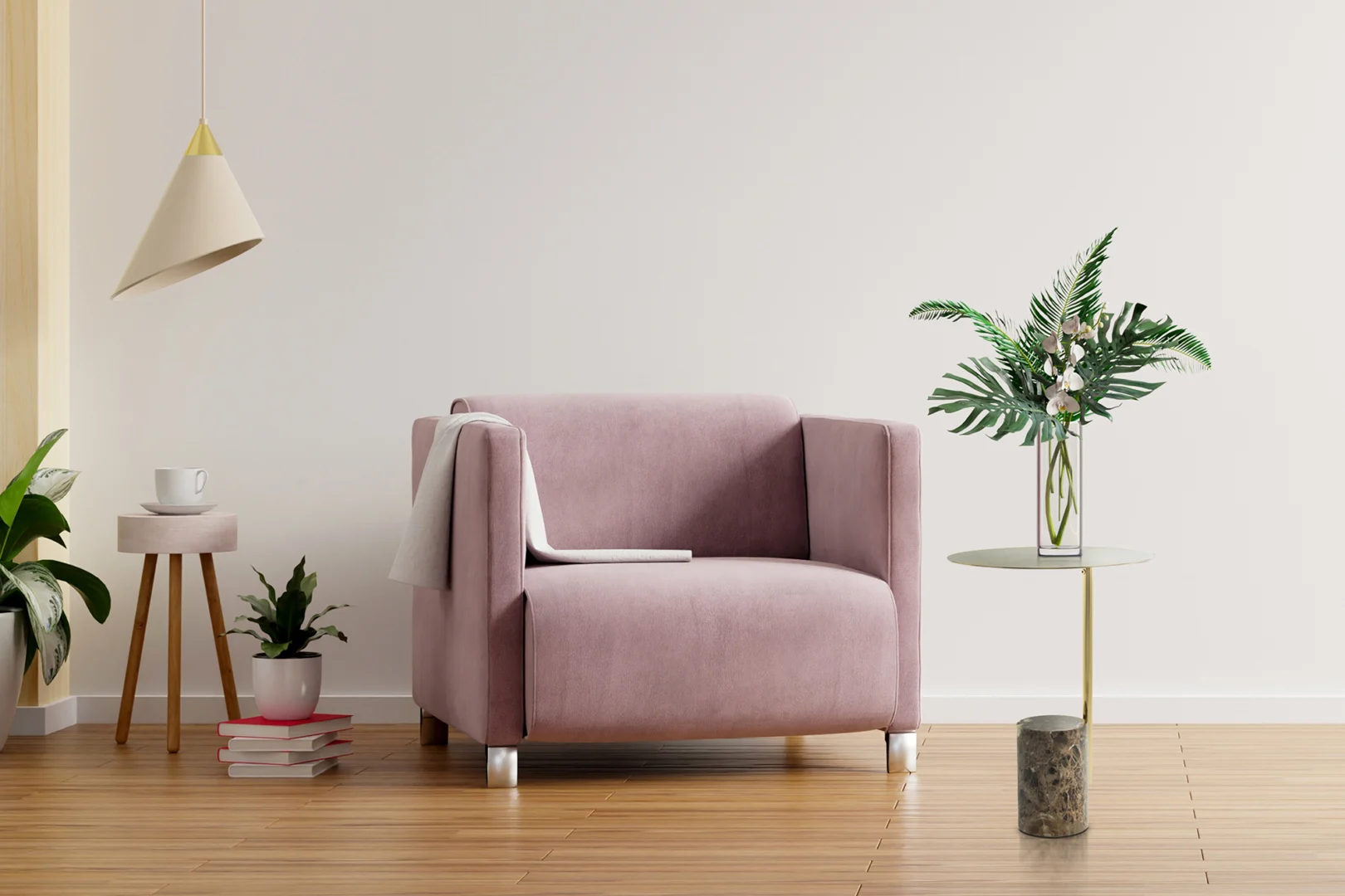 Een moderne woonkamer met een roze fauteuil, een witte hanglamp, de Bijzettafel Bruin Rond Marmer Chique met een vaas van groene bladeren, potplanten, gestapelde boeken en een kopje op een lichte houten vloer tegen een effen witte muur.