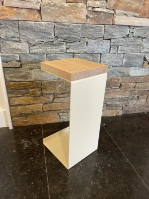 De Meni20 - Standaard heeft een modern ontwerp met een crèmekleurig metalen frame en houten blad, afgebeeld op zwarte tegels tegen een gestapelde grijze en bruine stenen muur.