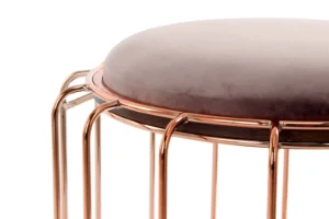 Een close-up van de Bijzettafel Glas, met een rond, pluche, lichtgrijs kussen en een glanzend roségoud metalen frame, weergegeven op een witte achtergrond.