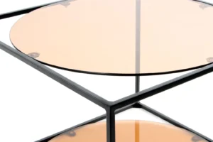 Close-up van de Bijzettafel Zwart Rond Metaal met een zwart metalen frame en een rond getint glazen blad en onderste plank, getoond vanuit een hoek die het moderne ontwerp benadrukt.