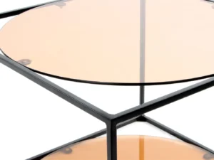 Close-up van de Bijzettafel Zwart Rond Metaal met een zwart metalen frame en een rond getint glazen blad en onderste plank, getoond vanuit een hoek die het moderne ontwerp benadrukt.