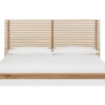 Vooraanzicht van een platformbed van massief essenhout met lattenbodem hoofdeinde en wit beddengoed tegen een witte achtergrond.