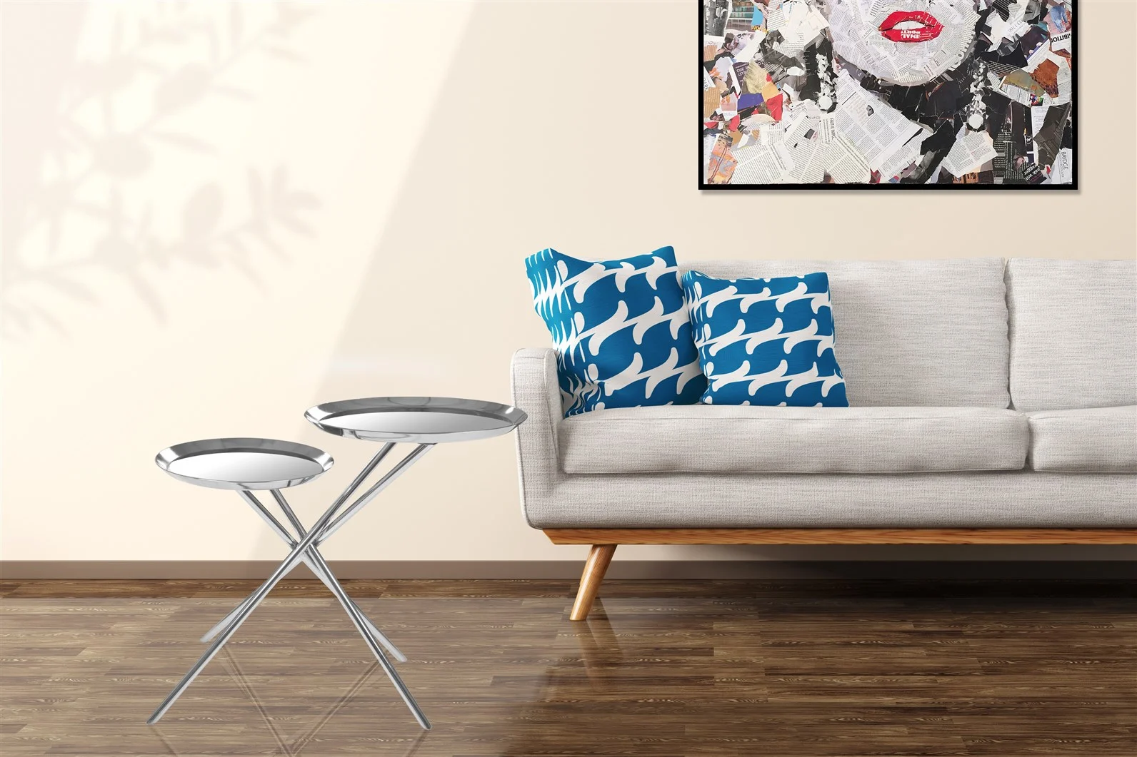Een moderne woonkamer met een lichtgrijze bank, kussens met blauwe en witte patronen, twee Bijzettafel Zilver Rond Ijzer Design bijzettafels, een houten vloer en een muurprint met een collage van rode lippen.