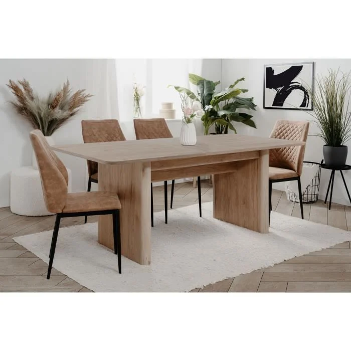 Een moderne eetkamer met de Uitschuifbare tafel SAI (rechthoekig, Jackson Hickory, 10 zitplaatsen), vijf tan gestoffeerde stoelen met zwarte poten, een wit vloerkleed, decoratieve planten, abstracte kunst en een neutrale inrichting in een lichte, luchtige ruimte.