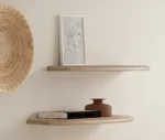Twee SENTO BOEKENPLANK120 WWM lichthouten zwevende planken op een crèmekleurige muur: op de bovenste plank staat een minimalistische lijntekening van een vrouwenprofiel; op de onderste staan gestapelde boeken en een kleine bruine vaas. Links hangt een geweven wandmand.