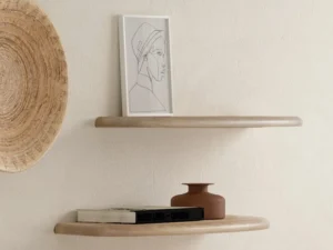 De SENTO BOEKENPLANK80 WWM minimalistische zwevende planken op een beige muur tonen een ingelijste lijntekening, boeken en een kleine bruine vaas. Naast de bovenste plank is een geweven mand gemonteerd voor extra decoratieve aantrekkingskracht.