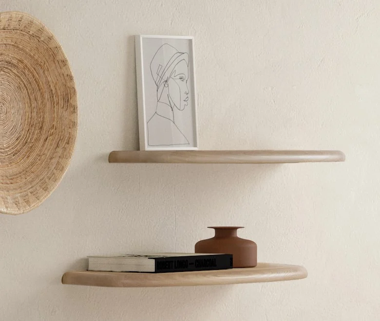 De SENTO BOEKENPLANK80 WWM minimalistische zwevende planken op een beige muur tonen een ingelijste lijntekening, boeken en een kleine bruine vaas. Naast de bovenste plank is een geweven mand gemonteerd voor extra decoratieve aantrekkingskracht.