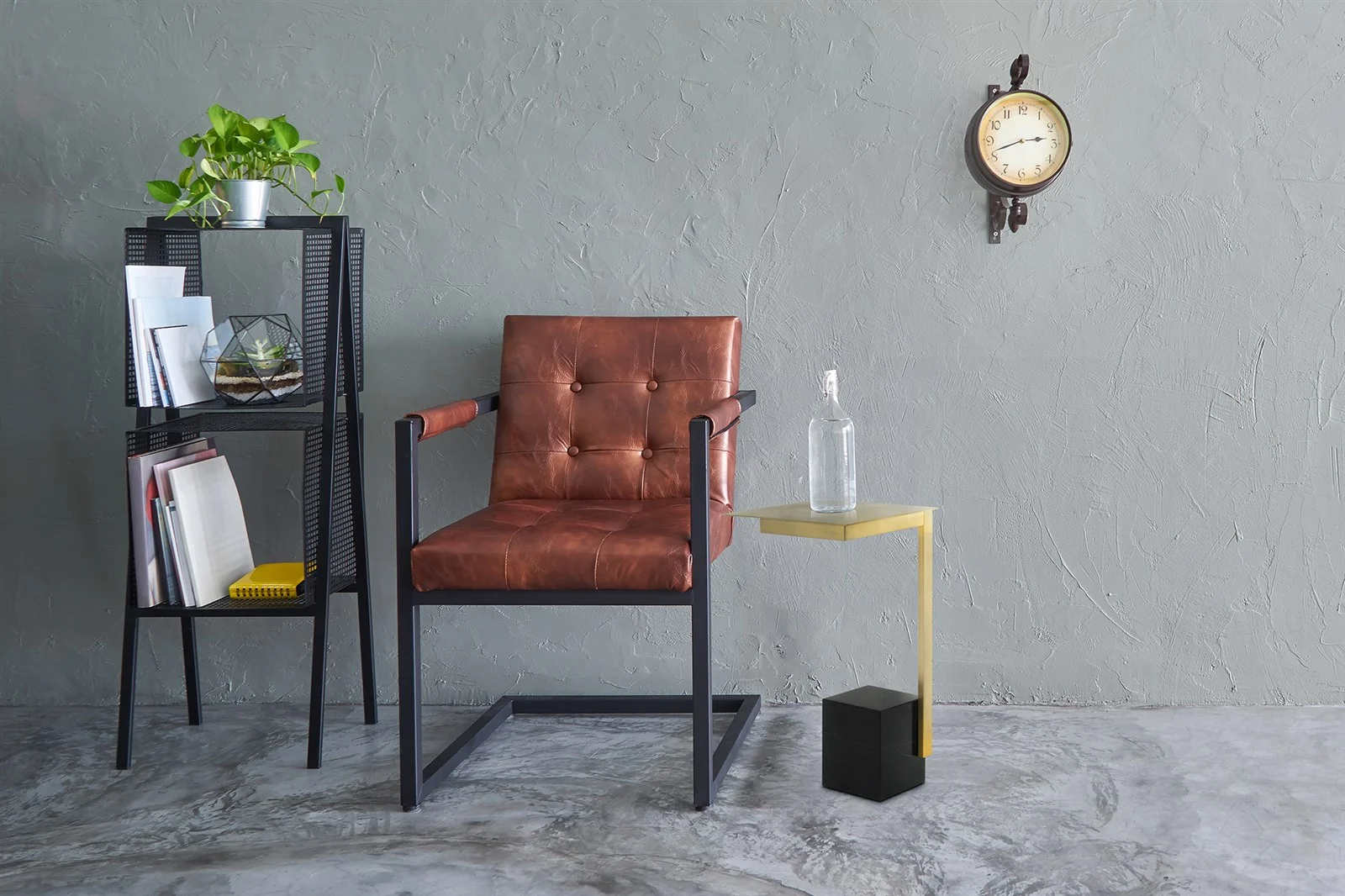 Een modern interieur met een bruine leren stoel, de Bijzettafel Zwart Vierkant Marmer ernaast, een zwarte plank met boeken en een potplant en een vintage wandklok op een grijze muur met structuur.