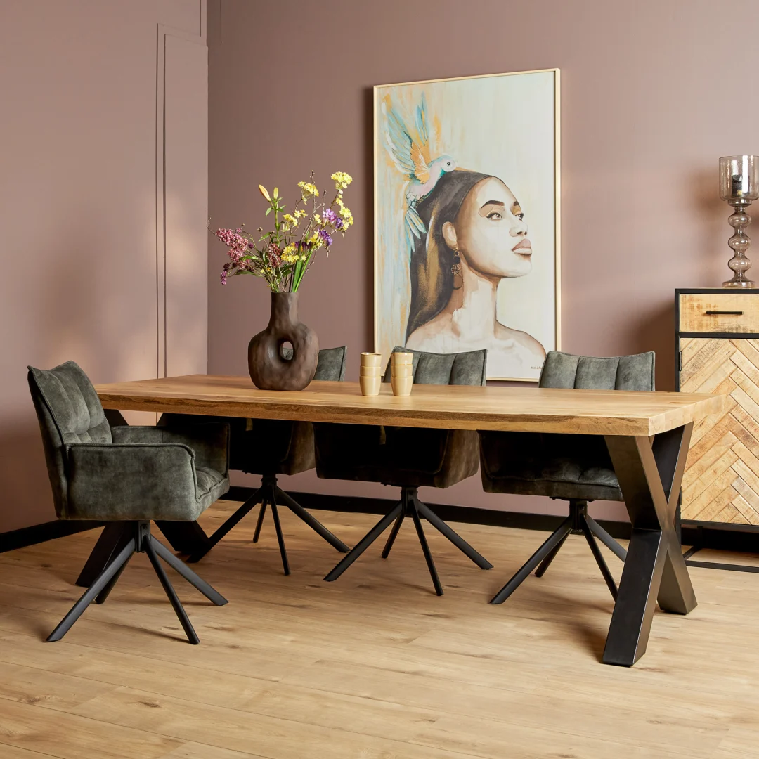 Een moderne eetkamer met de Eettafel Denver | Rechthoek X-poot | 240 cm, vier groene stoelen met kussens en zwarte poten, een vaas met bloemen, kopjes van keramiek, een stijlvolle kast en een groot schilderij van een vrouw met een gevederde hoofdtooi.