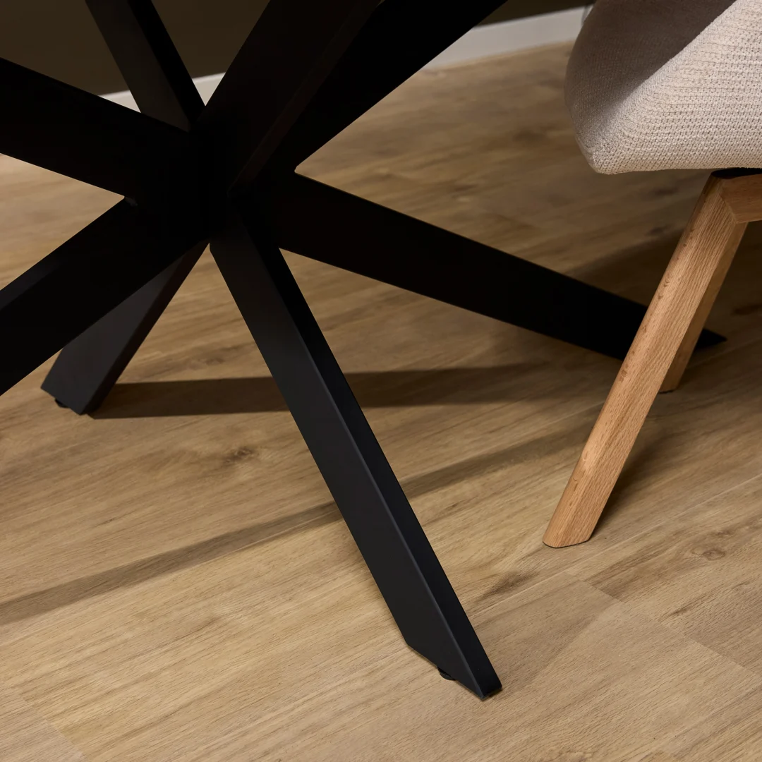 Detail van een eikenhouten eettafel met een zwart metalen onderstel en een stoel. Lichte houten vloer, warme belichting.