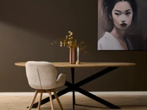 Ovale eikenhouten eettafel met zwart metalen onderstel, beige stoel, vaas en schilderij tegen een donkerbruine achtergrond. Mooi interieur.