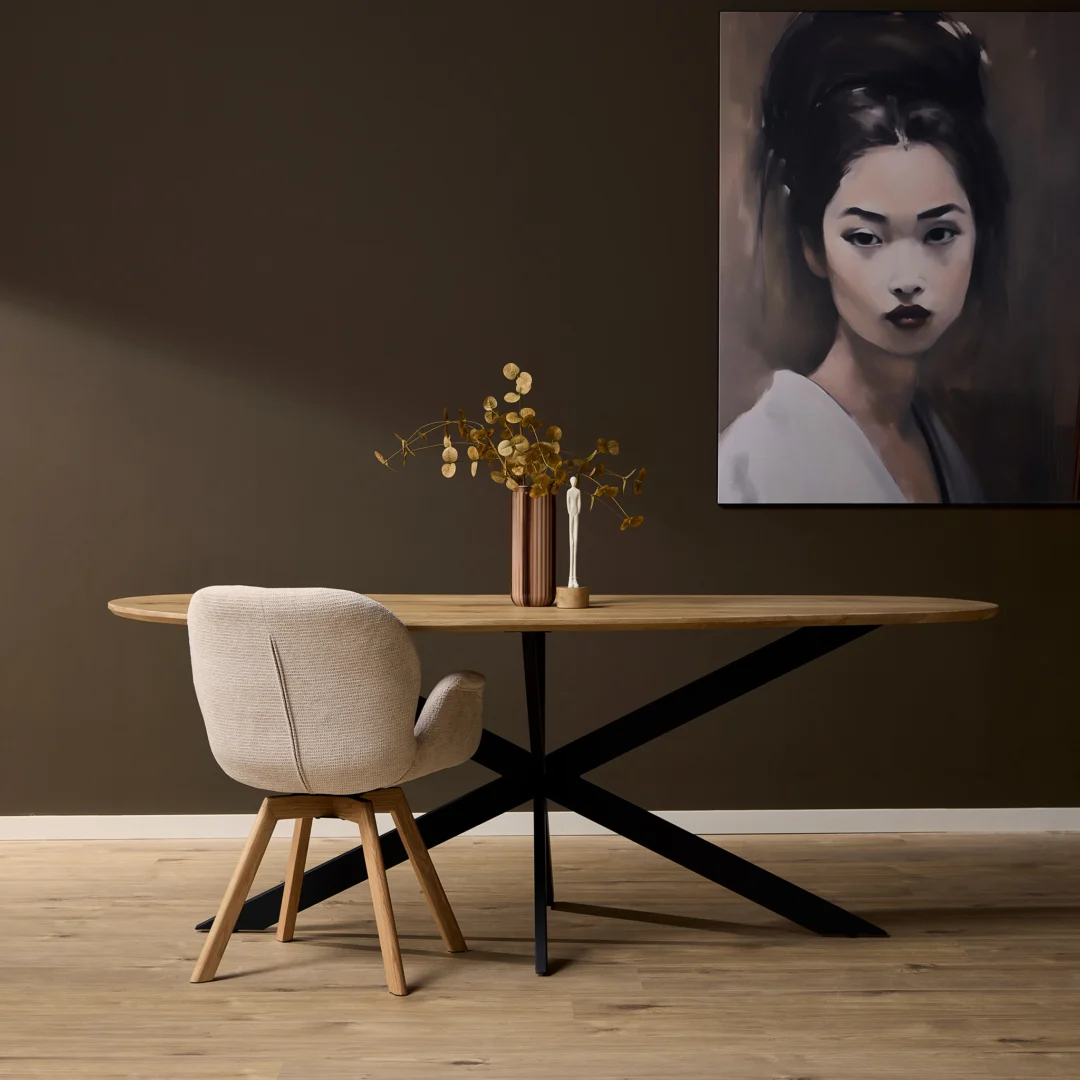 Studiofoto van een ovale eikenhouten eettafel met een zwart metalen onderstel. Een beige stoel en een schilderij op de donkerbruine achtergrond.