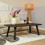 Een moderne woonkamer met een beige bank, Salontafel Zwart 70 x 45 CM Design salontafel, een vaas met roze en witte bloemen, twee kopjes, een vloerkleed met patroon en een staande lamp met een geweven kap.