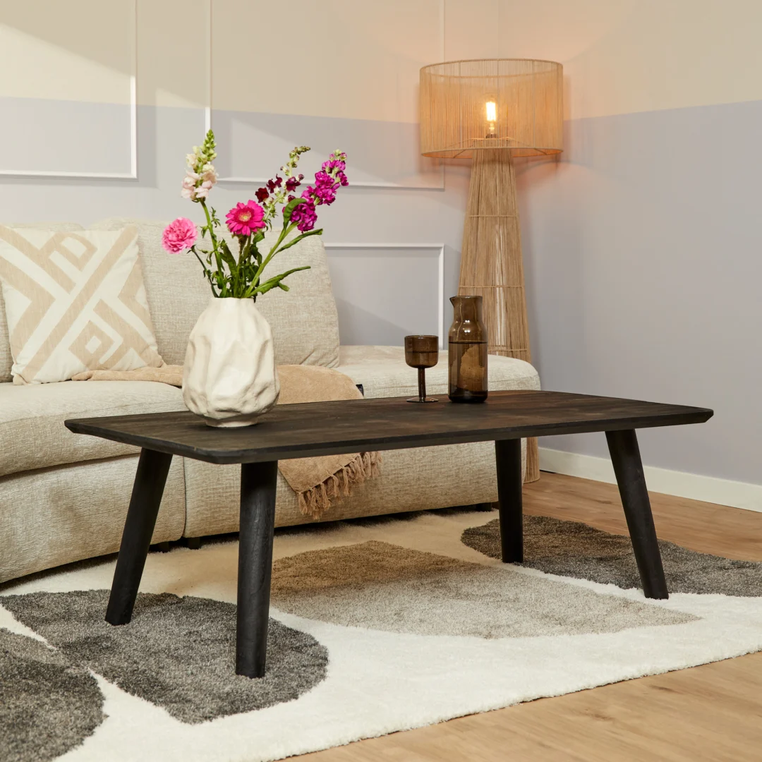 Een moderne woonkamer met een beige bank, Salontafel Zwart 70 x 45 CM Design salontafel, een vaas met roze en witte bloemen, twee kopjes, een vloerkleed met patroon en een staande lamp met een geweven kap.