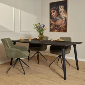 Een moderne eethoek met de Eettafel Omaha Zwart (200 cm) donker houten tafel, vier groen gestoffeerde stoelen, een vaas met bloemen, servies en een portret van een vrouw en een uil boven een licht houten vloer.