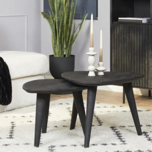 Een Salontafel Zwart 66 x 56 CM Vierkant ligt op een wit gedessineerd tapijt. Drie witte kaarsen in houders staan op tafel, met een groene potplant op de achtergrond bij een witte bank.