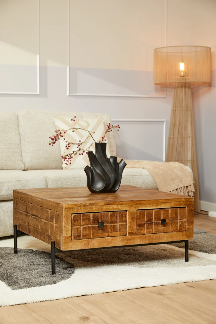 Een gezellige woonkamer met een lichte bank, de Salontafel 80 x 80 CM Vierkant salontafel met laden en zwarte poten, een zwarte vaas met rode bessen, een staande lamp met geweven kap en een beige plaid.
