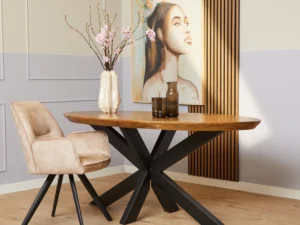Een moderne eethoek met de Eettafel Brandy Ovaal 180 cm houten tafel met een zwart metalen onderstel, een beige gestoffeerde stoel, roze bloemen in een vaas, wandkunstwerk van een vrouw met een vogel, lichthouten vloeren en wanden met lambrisering.