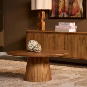 Houten salontafel roest kleur, rond design. Zijaanzicht, warme tinten, decoratieve objecten erop. Houten vloer en kast op de achtergrond.