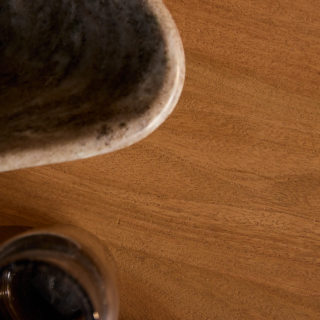 Bovenaanzicht van een houten eettafel in naturel tinten met een kom en glas. Het warme licht accentueert de textuur van het hout.