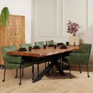 Een moderne eetkamer met de Boomstamtafel Boston 300 cm, groene stoelen met kussens, zwart servies, een houten kast, een varen in pot en een vaas met rood gebladerte op een beige sokkel.