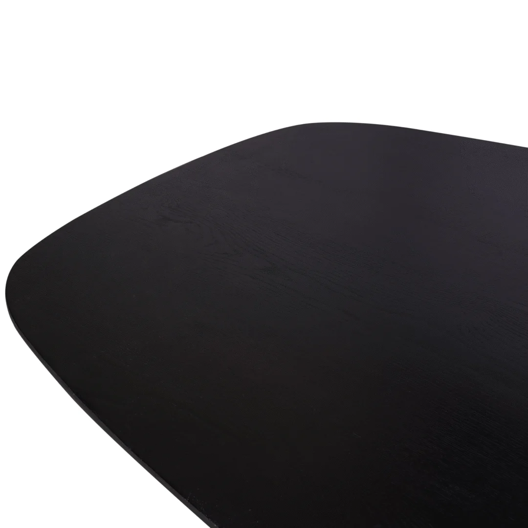Close-up van de hoek van de Eiken eettafel Ferris | Deens Ovaal 240 cm | Zwart, met een gladde, licht gebogen donkere houten rand tegen een witte achtergrond.