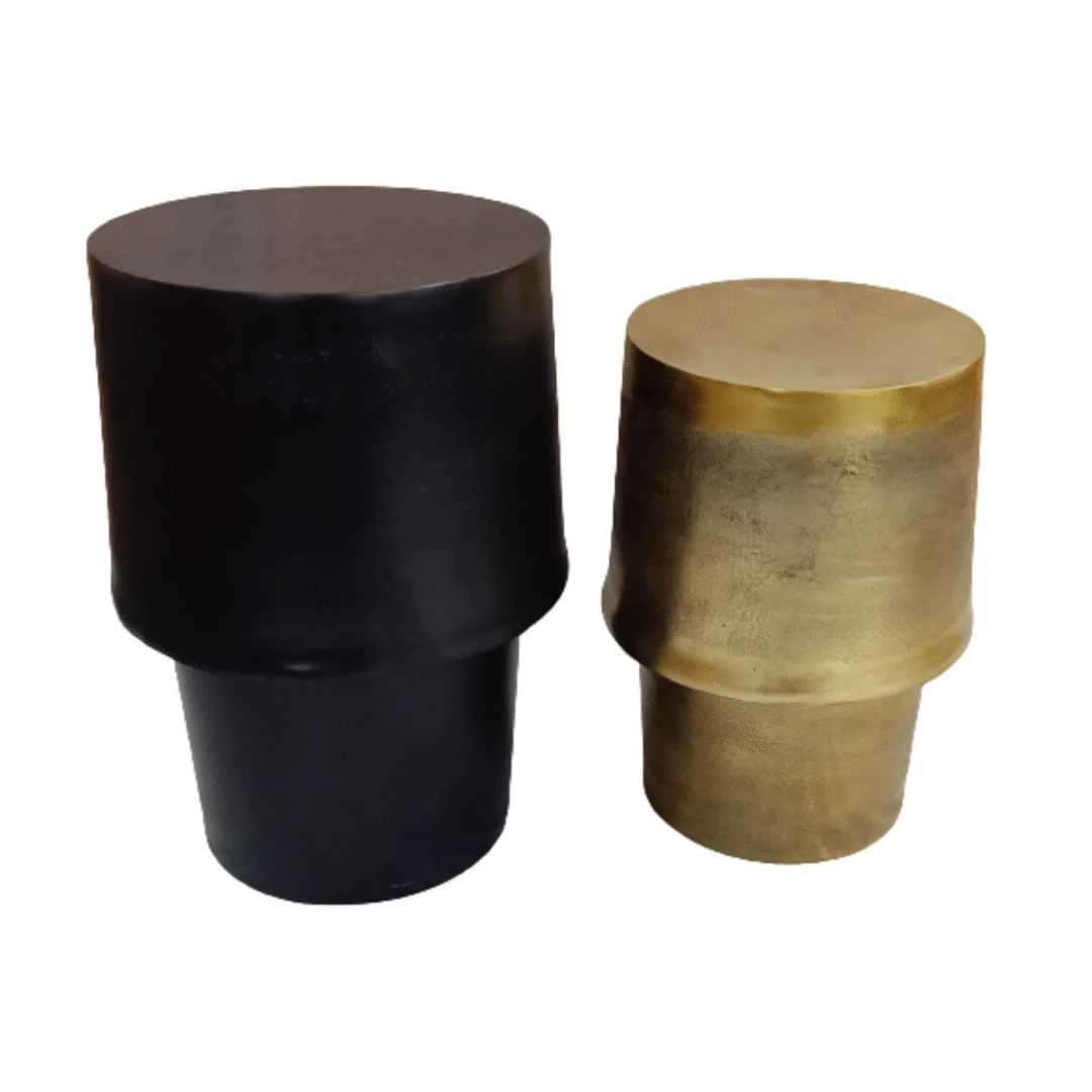 Twee bijzettafels van Kacy met brede cilindrische voet - één zwart, één goud - staan naast elkaar op een witte achtergrond. Hun eenvoudige, moderne ontwerp heeft gladde oppervlakken.