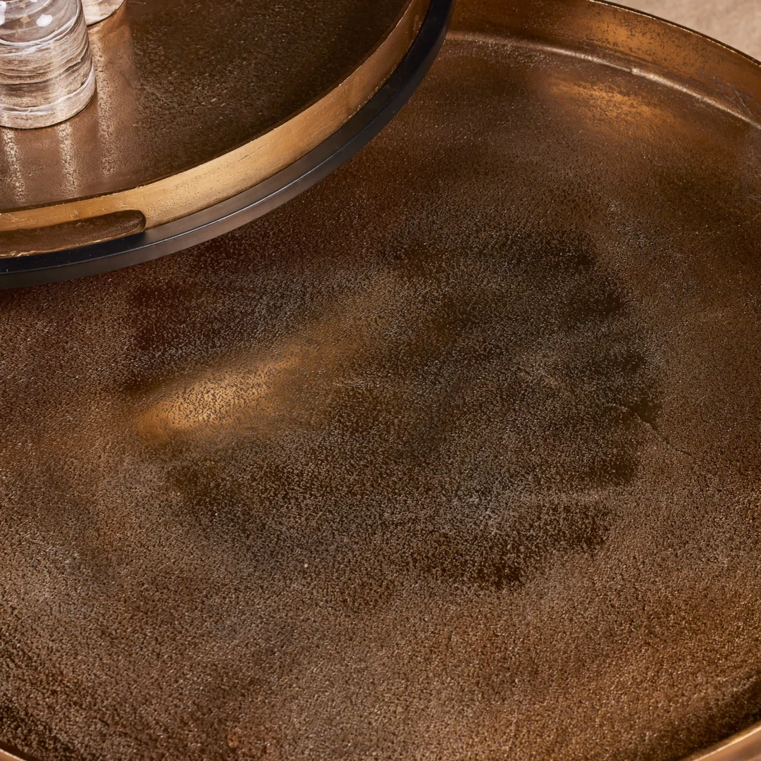 Een close-up van de Salontafel 78 x 37 CM Vierkant benadrukt het bronskleurige metalen oppervlak met een subtiel structuurpatroon, met twee dienbladen - het ene meestal leeg, het andere met glazen bekers.