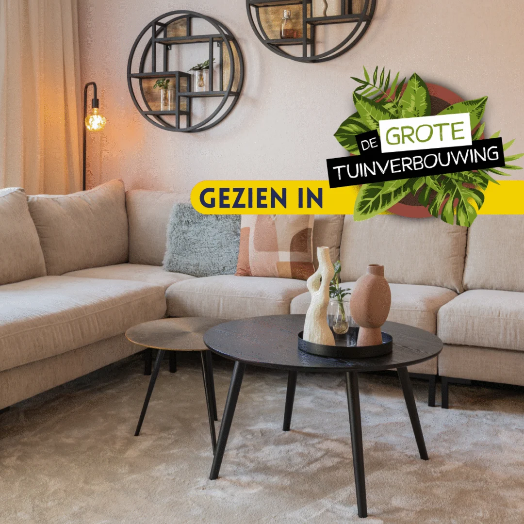 Een gezellige woonkamer met een beige zitbank, Bijzettafel set Ryas (ronde zwarte tafels), decoratieve vazen, wandplanken en een zacht vloerkleed. Tekst overlay: GEZIEN IN DE GROTE TUINVERBOUWING met bladafbeeldingen.