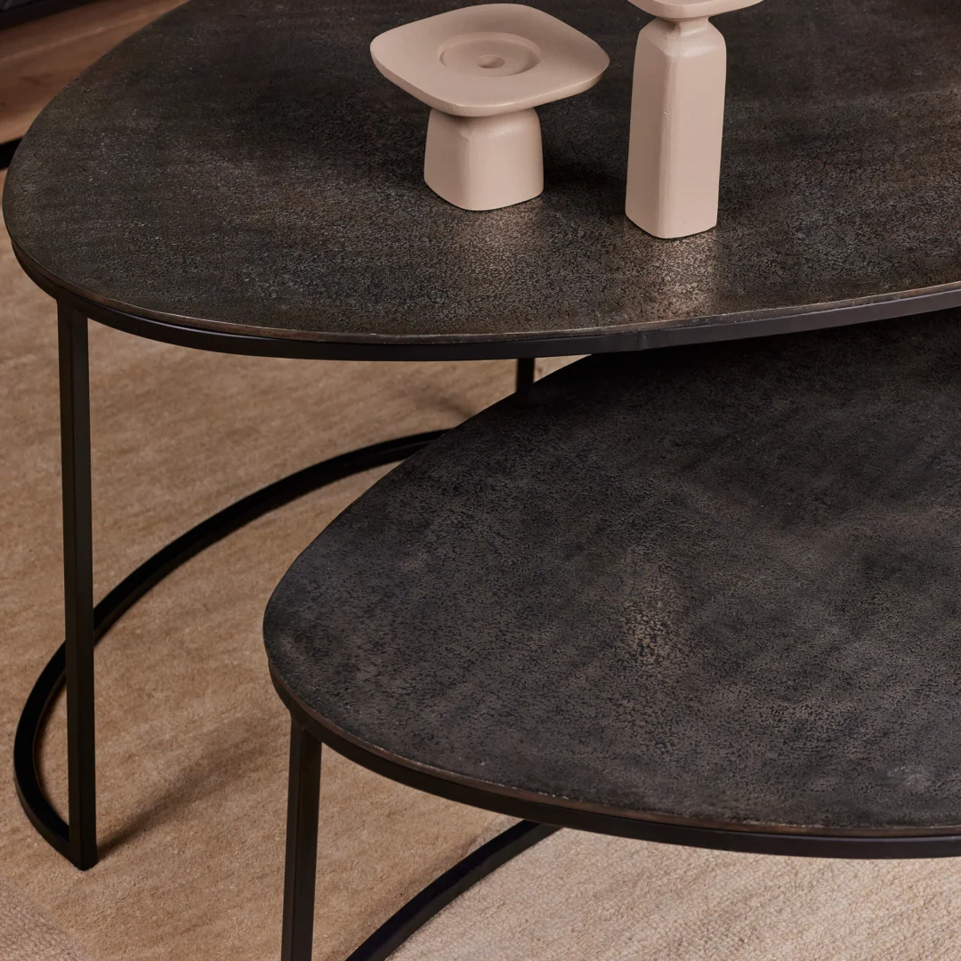 De Salontafel 65 x 50 CM, met een donker gestructureerd oppervlak en slanke zwarte metalen poten, staat op een beige vloerkleed met lichtgekleurd keramiekdecor erop.