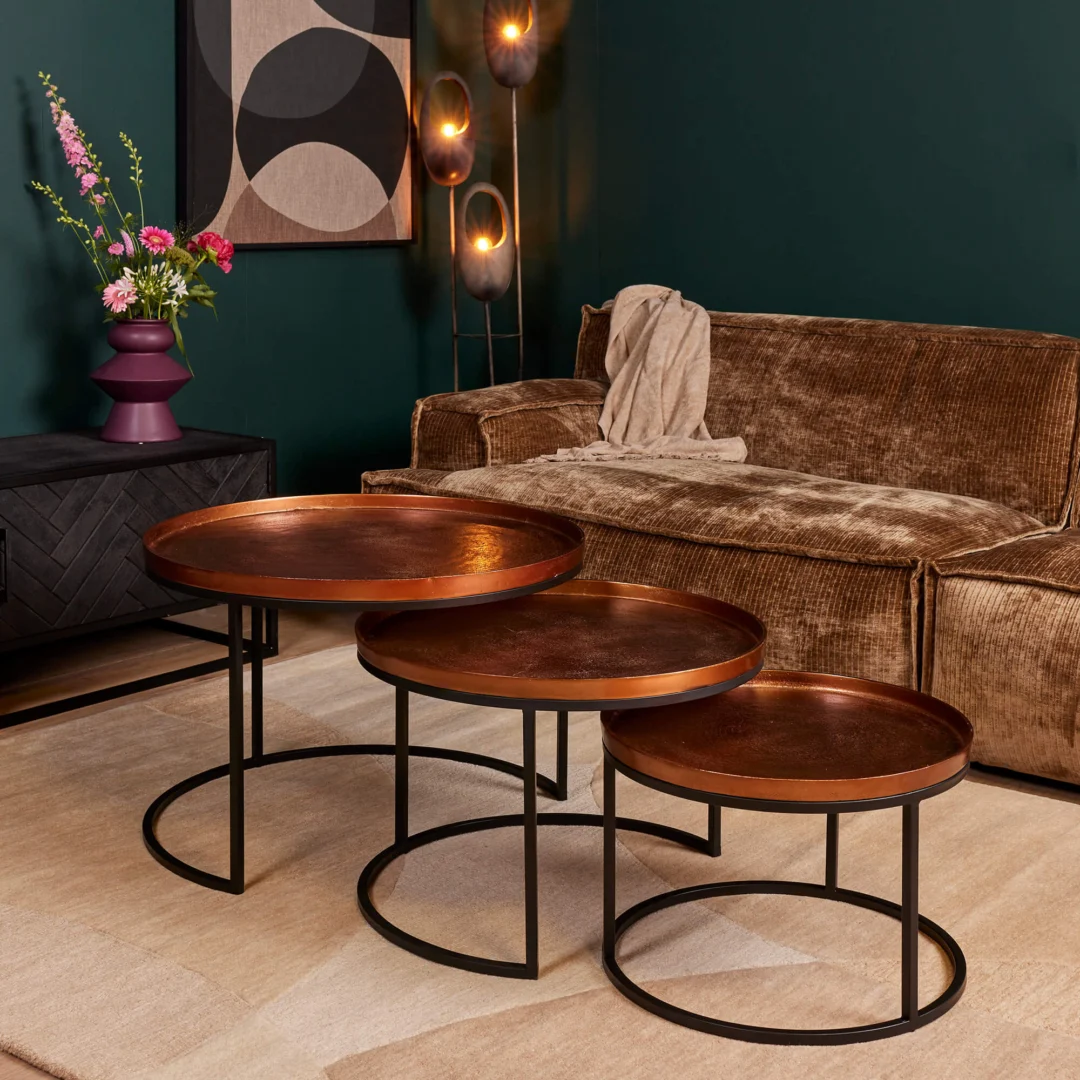 Een moderne woonkamer met een bruin fluwelen bank, een Salontafel 50 CM Vierkant, beige vloerkleed, bloemenvaas op een zwarte kast, abstracte muurkunst en hoge staande lampen tegen een donkergroene muur.