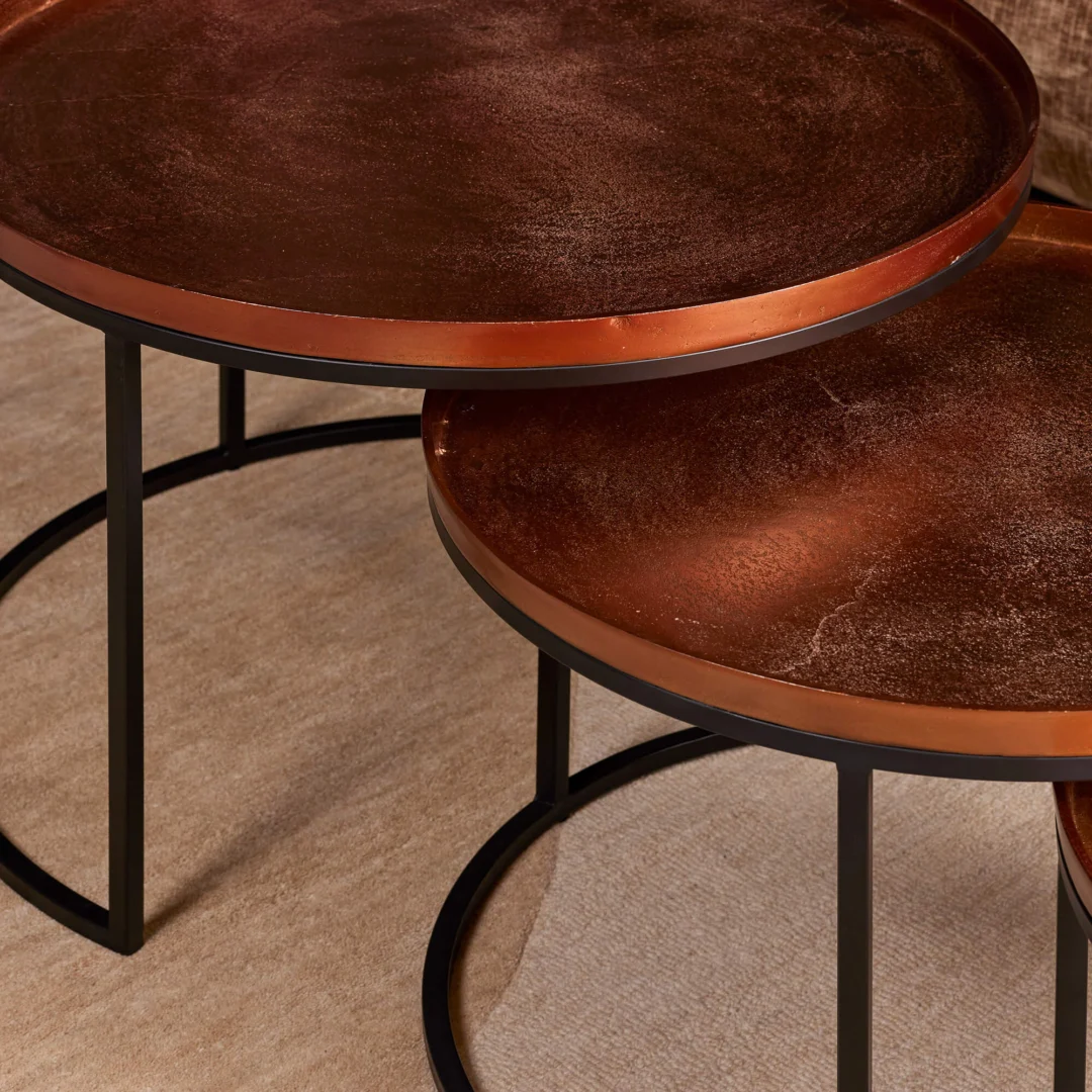 De Salontafel 50 CM Vierkant bestaat uit twee ronde nesttafels met donker koperen bladen en zwart metalen poten, op een beige tapijt. De kleinere tafel is gedeeltelijk weggestopt onder de grotere.