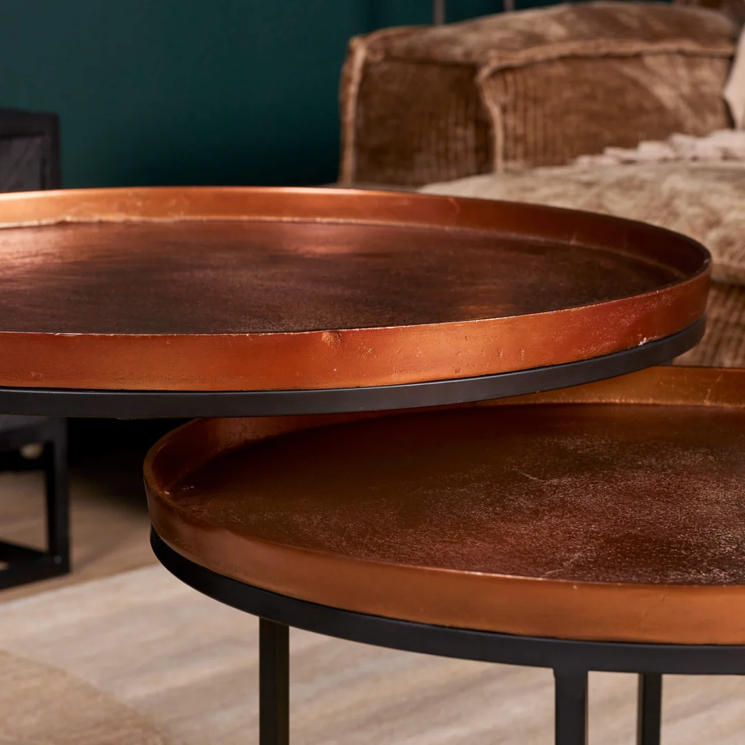 Close-up van een Salontafel 50 CM Vierkant met een koperkleurig metalen dienblad en zwarte poten, in een gezellige woonkamer met een beige bank en een groene muur op de achtergrond.