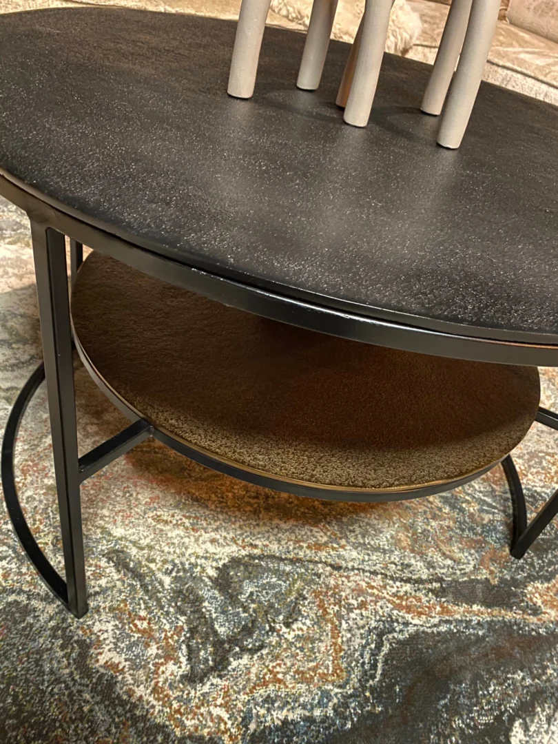 De Salontafel Zwart, Goud 80 x 80 CM is een vierkante salontafel op een gedessineerd kleed. Hij heeft metalen poten, een zwart blad met een bruine onderste plank en is versierd met een decoratief object van verticale stangen.