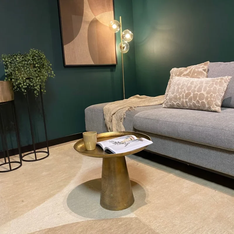 Een moderne woonkamer met een grijze bank, kussens met patroon, een beige kleed, een Salontafel 50 x 50 CM Vierkant met een mok en een tijdschrift, een potplant, abstracte muurkunst en een staande lamp met drie gloeilampen.