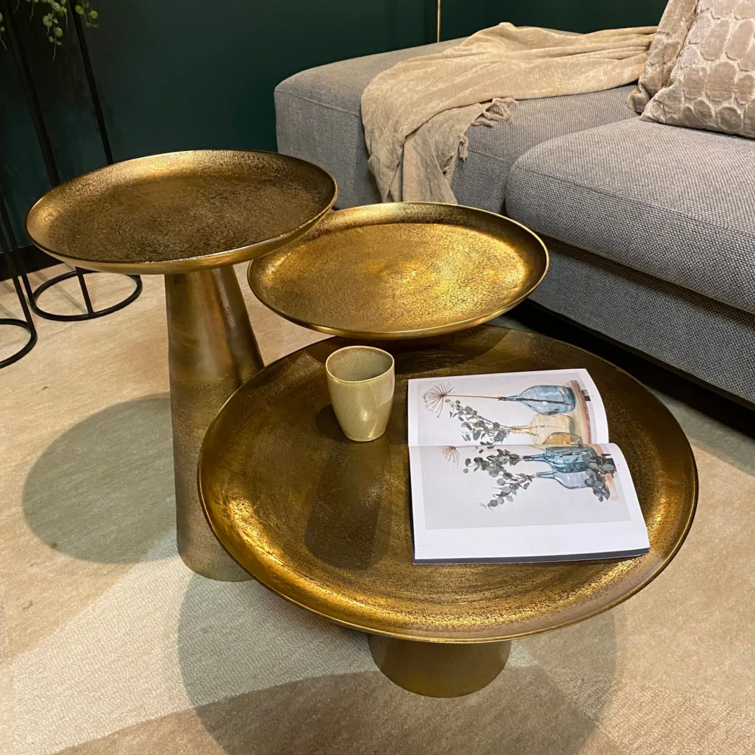 Een Salontafel 50 x 50 CM Vierkant staat in een woonkamer bij een grijze bank met een beige kleed; op tafel staan een beige kopje en een open tijdschrift met een bloemenillustratie.