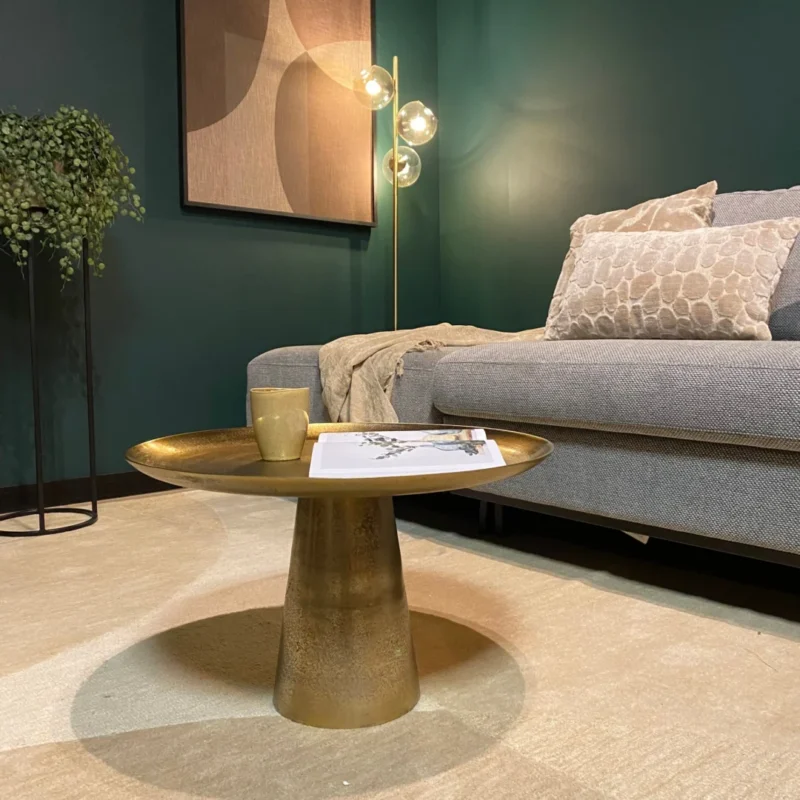 Een moderne woonkamer met een grijze bank, gedessineerde kussens, een pluche beige vloerkleed, een Vierkant Salontafel 58 x 36 CM met een mok en een tijdschrift, een staande lamp met gloeilampen, een hangplant en abstracte muurkunst.