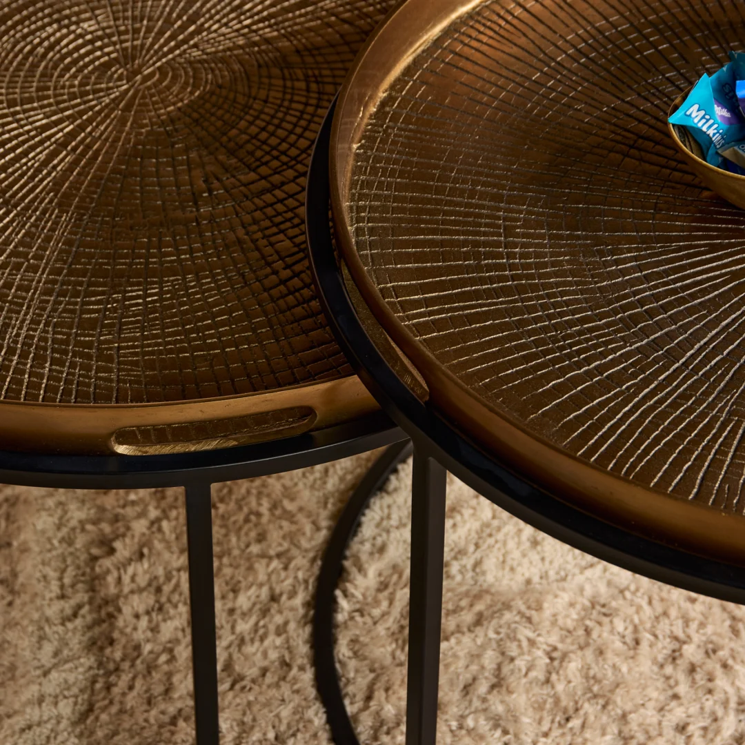 Detailopname van een gouden salontafel set met zwarte poten. Het blad heeft een uniek, cirkelvormig patroon. Zacht licht.