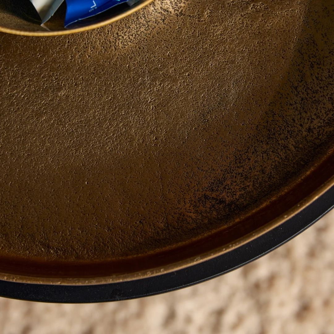 Bovenaanzicht van een design bijzettafel. Gouden blad met een ruwe textuur en een zwarte rand. Zachte, natuurlijke belichting.