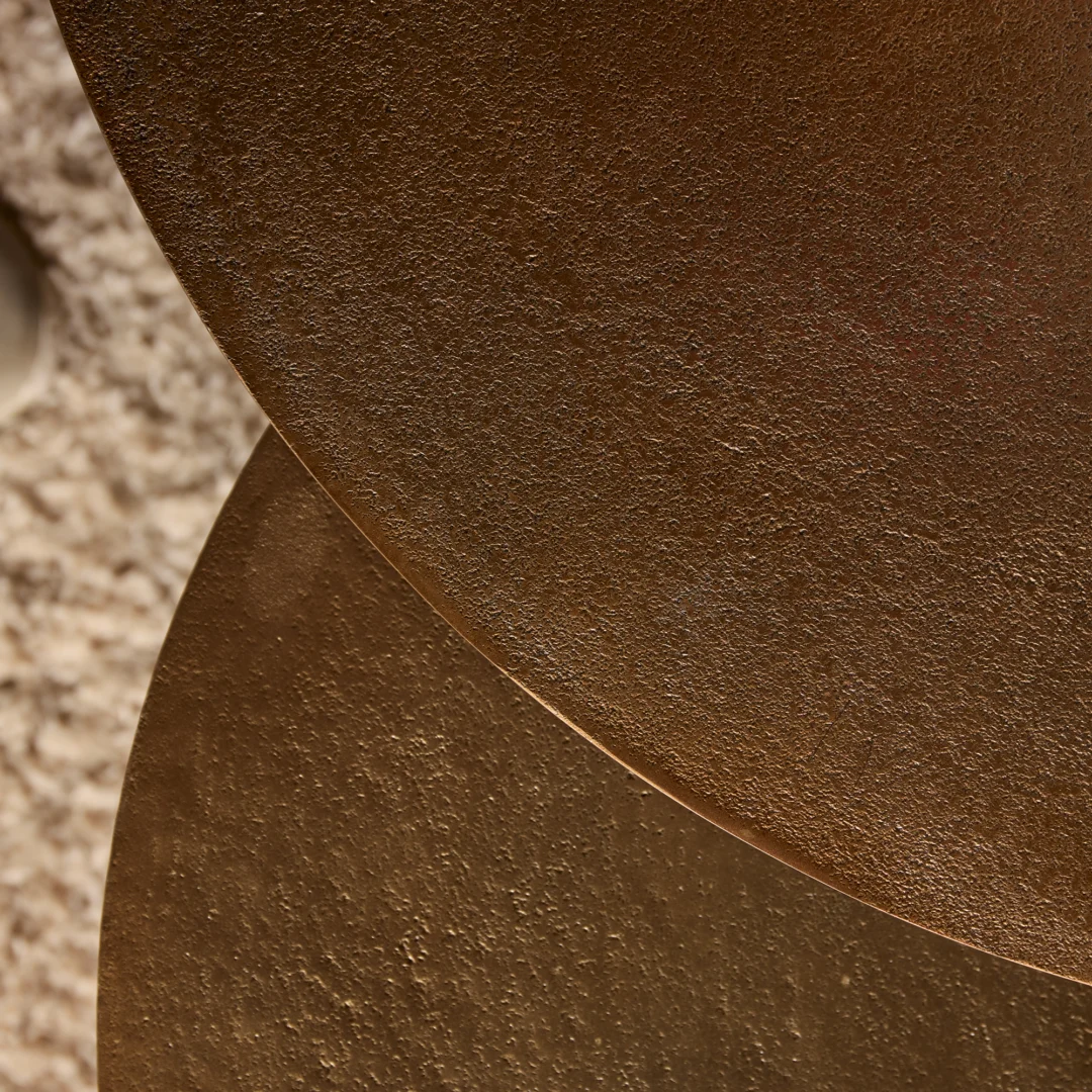 Close-up van een goudkleurige salontafel, toont de textuur en het warme licht. De ronde vorm en het materiaal vallen op.