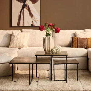 Drie roestkleurige salontafels met een metalen frame op een zacht, crèmekleurig vloerkleed. Een beige bank en decoratieve accessoires op tafel.